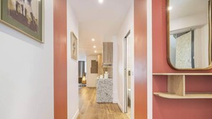 Un pasillo estrecho con encimera de mármol y un espejo a la derecha, que conduce a una zona de cocina con armarios de madera y un lavabo.