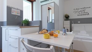 A modern kitchen with a dining table set for breakfast, including bread, pastries, and orange juice.