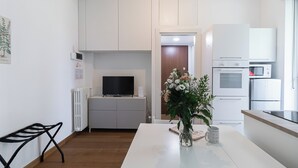 A modern kitchen with white cabinets, a built-in oven, microwave, and refrigerator. There's a dining table with a vase of flowers and a coffee mug.