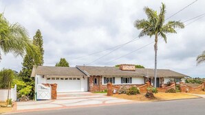 Une maison de plain-pied avec un garage, une façade en briques et un petit jardin devant, agrémenté de palmiers.