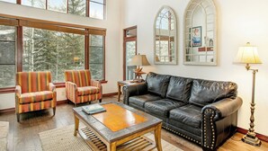 A spacious living room with large windows, a leather sofa, striped armchairs, and a coffee table.