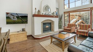 A spacious living room with a fireplace, comfortable seating, and a large window offering a view of a building with a sloped roof.