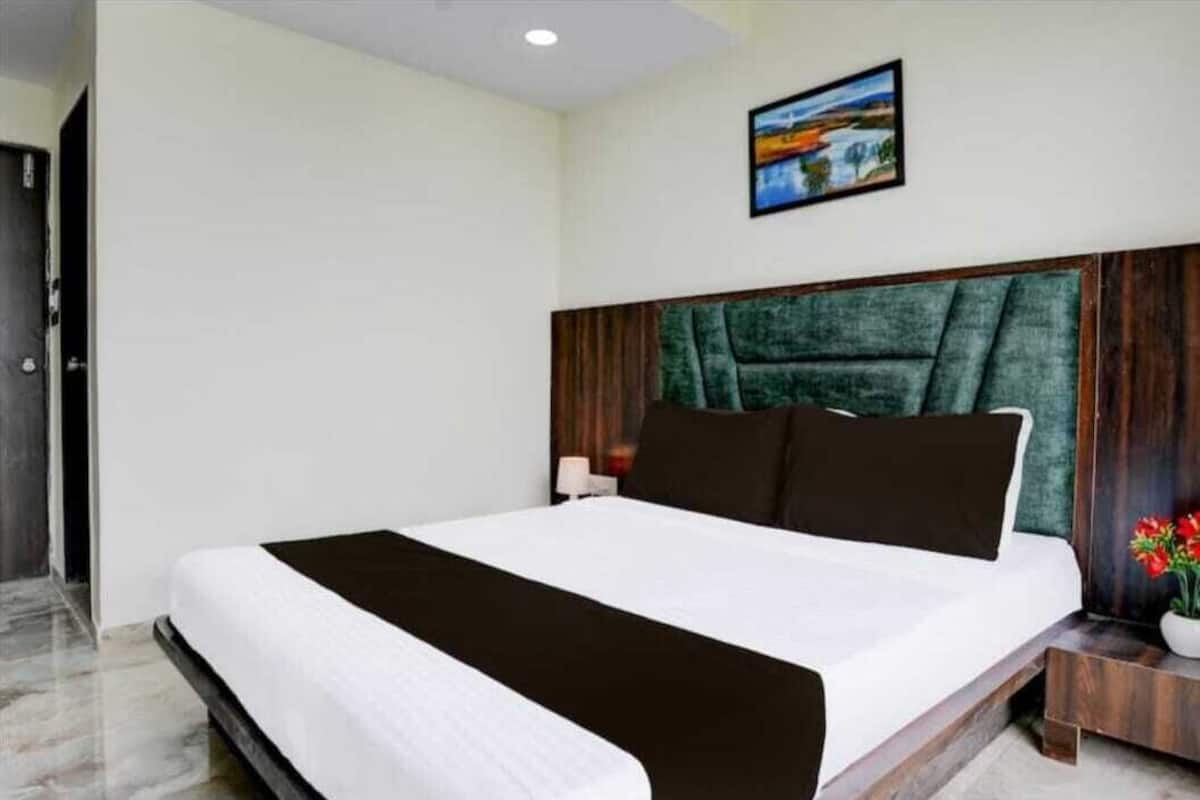 Quarto de hotel com uma cama grande, cabeceira de madeira, mesa de cabeceira e um quadro na parede.