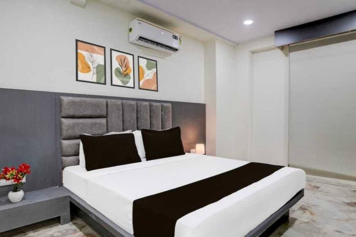 Quarto moderno com cabeceira acolchoada cinza, colcha branca e manta preta. Três obras de arte emolduradas na parede acima da cama.