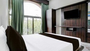 Ένα δωμάτιο ξενοδοχείου με ένα κρεβάτι, μια τηλεόραση τοποθετημένη στον τοίχο και ένα παράθυρο με κουρτίνες.