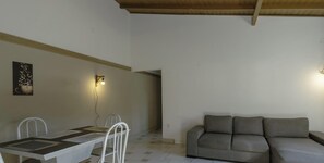 A dining area with a table and chairs, a grey sofa, and two wall-mounted lights. - Casa espaçosa a 200m da Praia em Florianópolis (Florianópolis)