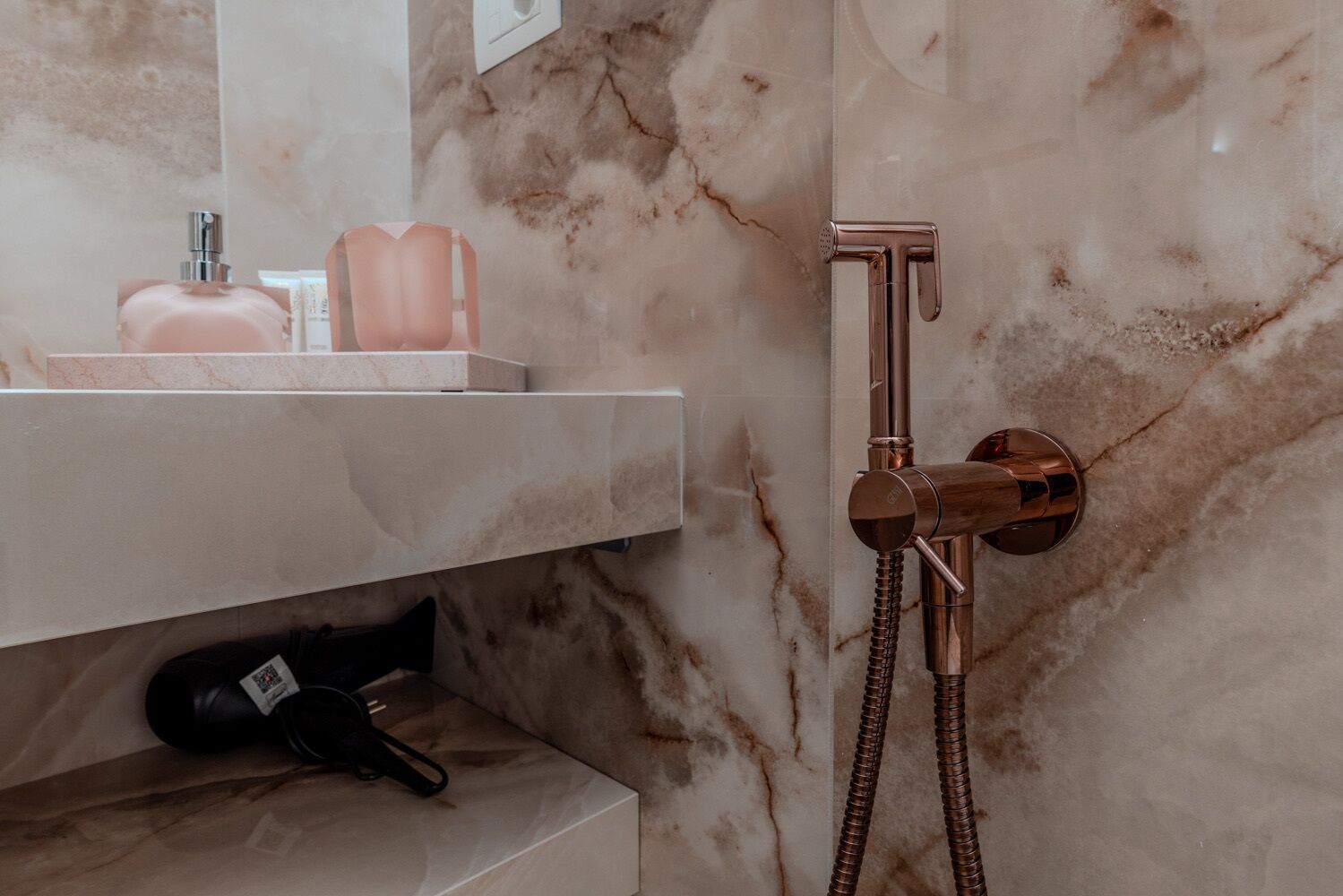 Un baño con pared de mármol, tocador blanco y ducha con cabezal de ducha de mano.