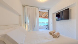 A hotel room with a bed, a TV mounted on the wall, and a view of the sea through a window.