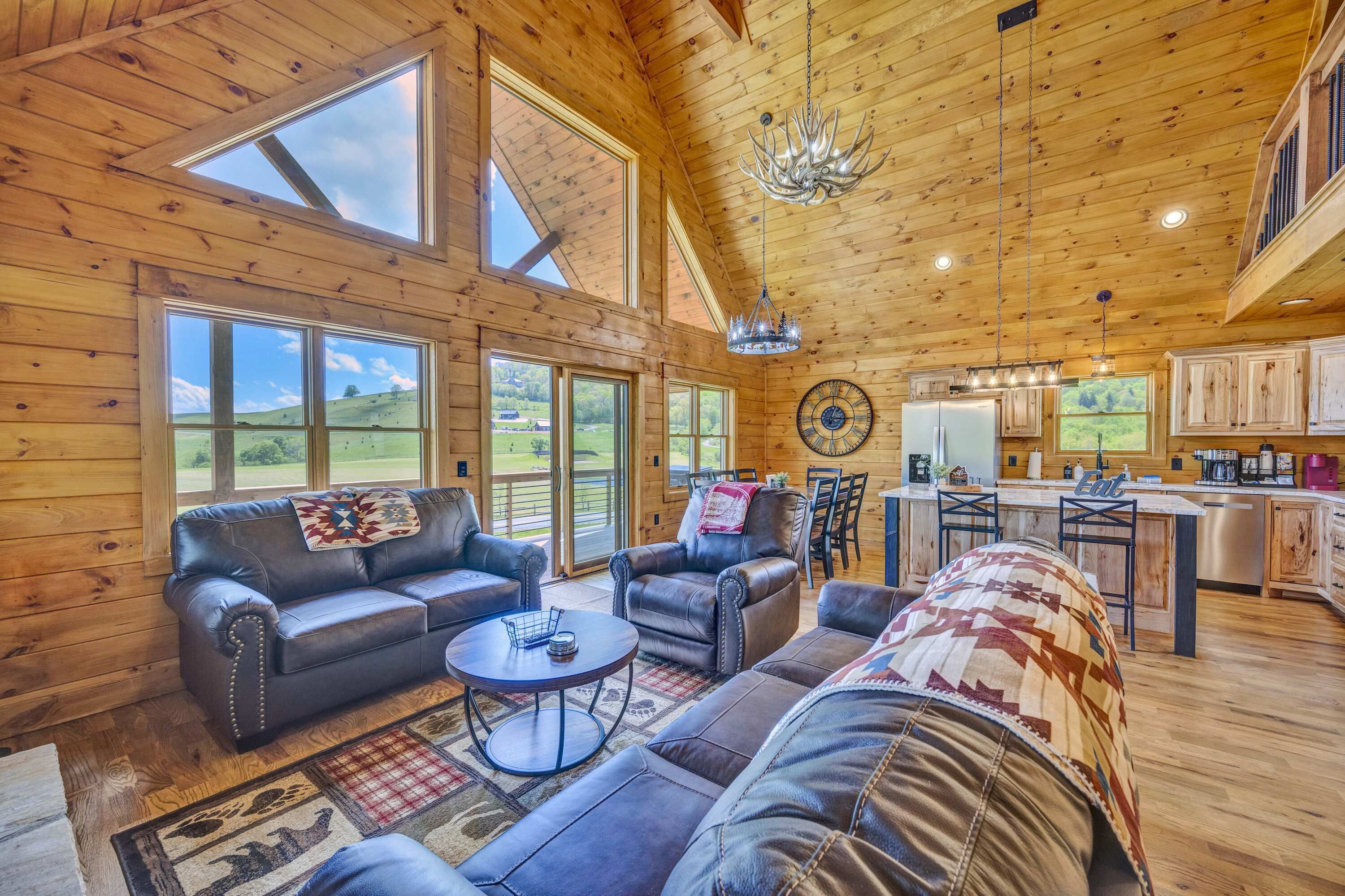 A spacious living room with leather sofas, a coffee table, and large windows offering a view of the outdoors.