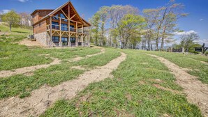 Une cabane en bois dotée d’une grande véranda et de nombreuses fenêtres, entourée d’un paysage verdoyant et d’arbres.