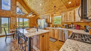Une cuisine spacieuse dotée de meubles en bois, d’un îlot en marbre et de grandes fenêtres offrant une vue sur l’extérieur.