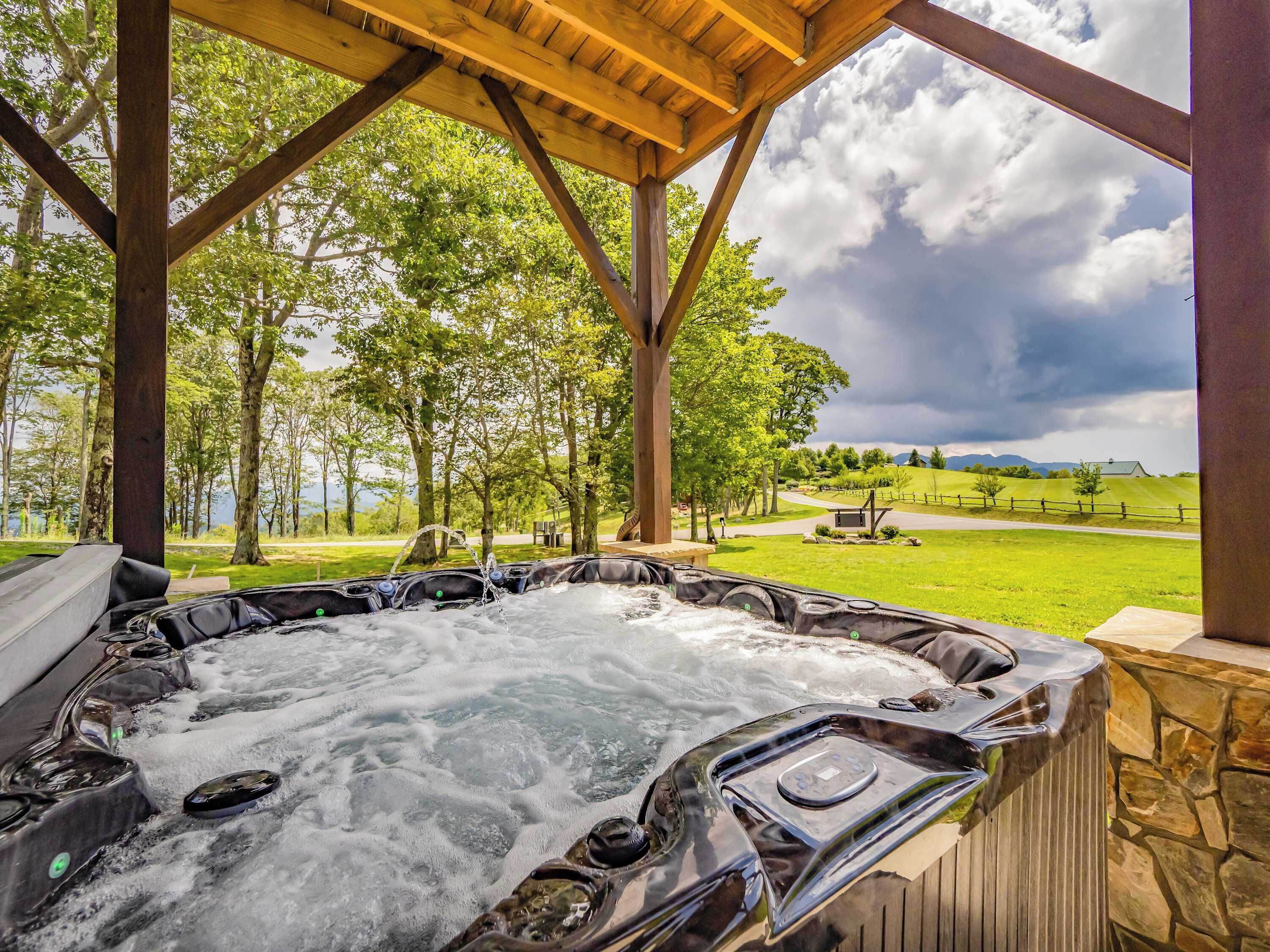 Un jacuzzi bajo una pérgola de madera con vistas a un campo cubierto de hierba y árboles.