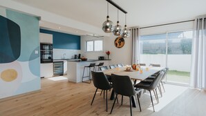 Une cuisine moderne avec un coin repas, de grandes fenêtres et une vue sur l’extérieur.