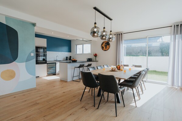 A modern kitchen with a dining area, large windows, and a view of the outdoors.