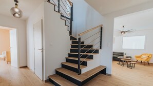 Un escalier moderne avec des marches en bois et des rampes en métal, menant à une pièce où se trouvent un canapé, un fauteuil jaune et une table.