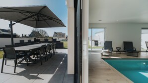 Un espace extérieur aménagé pour les repas, avec une table et des chaises, un grand parasol, et un coin détente au bord de la piscine avec des fauteuils.
