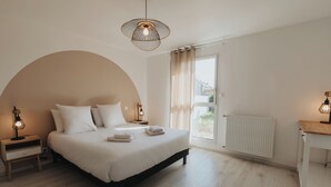 Une chambre à coucher avec un lit, des lampes de chevet, une table de chevet en bois, un radiateur et une vue sur l’extérieur.