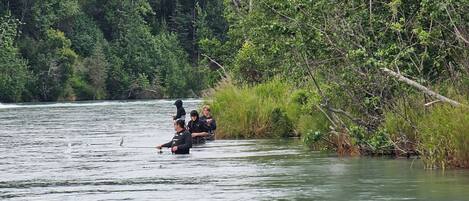 A group of people fishing in a river surrounded by dense greenery.