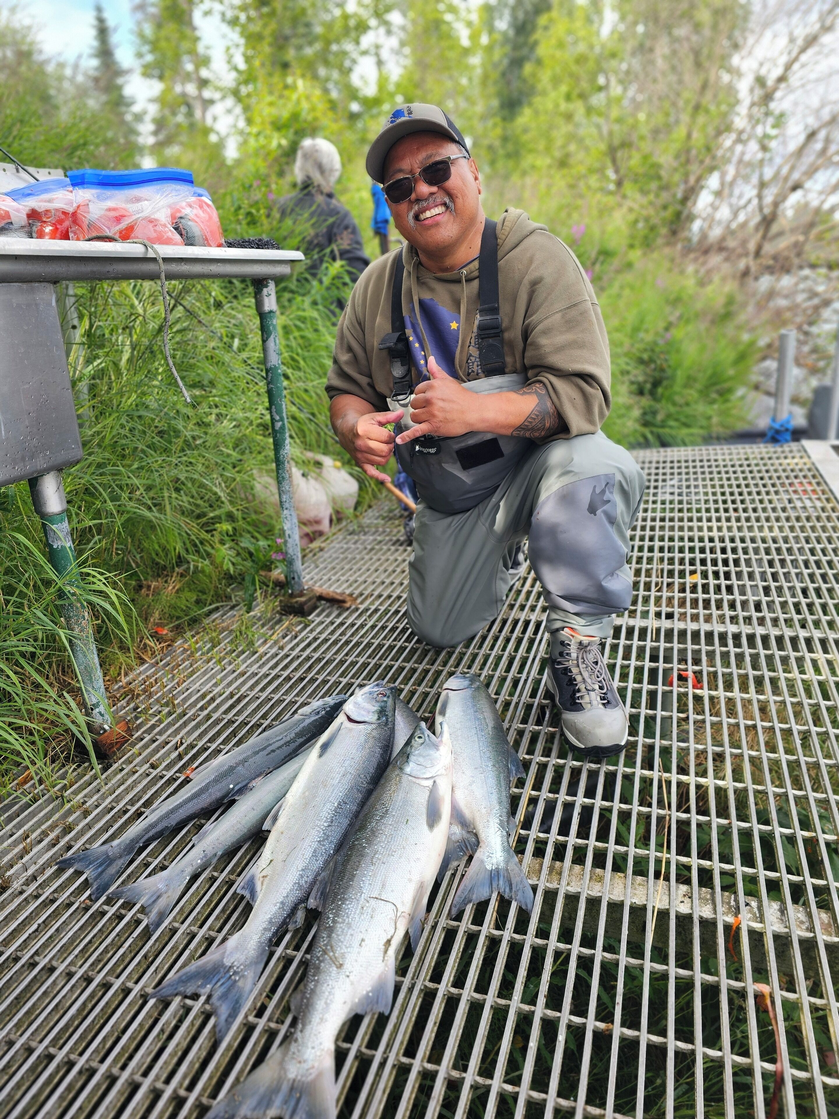 A person kneeling on a metal grill with several fish laid out in front.