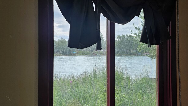 Een raam met uitzicht op een meer, gordijnen en een houten frame.
