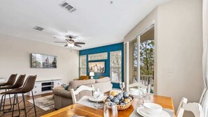 Un coin repas avec une table en bois dressée pour quatre personnes, un ventilateur de plafond et une vue sur l’extérieur.