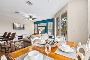 A dining area with a wooden table set for four, a ceiling fan, and a view of the outdoors.