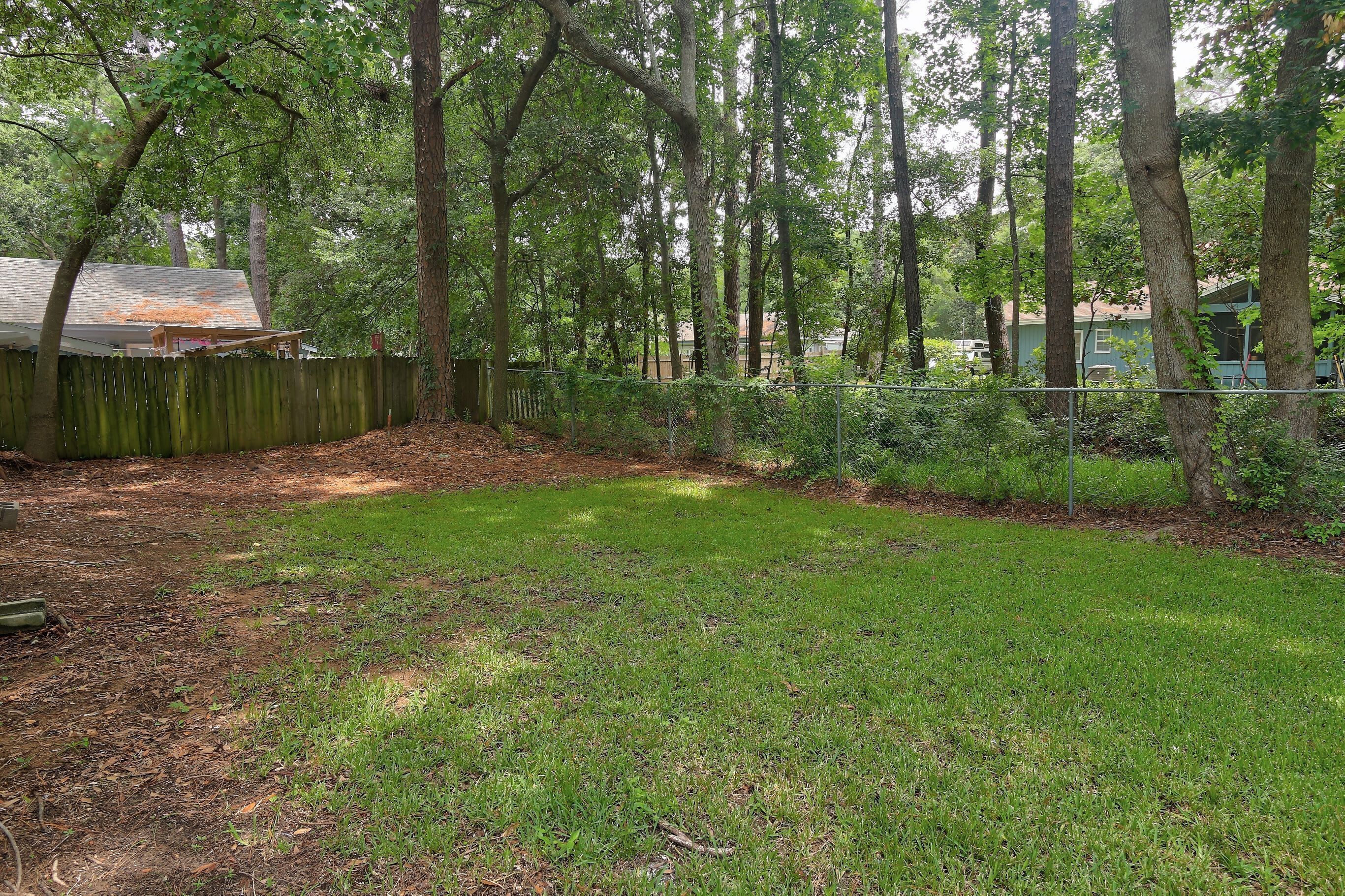 A fenced yard with trees, a wooden fence, and a grassy area.