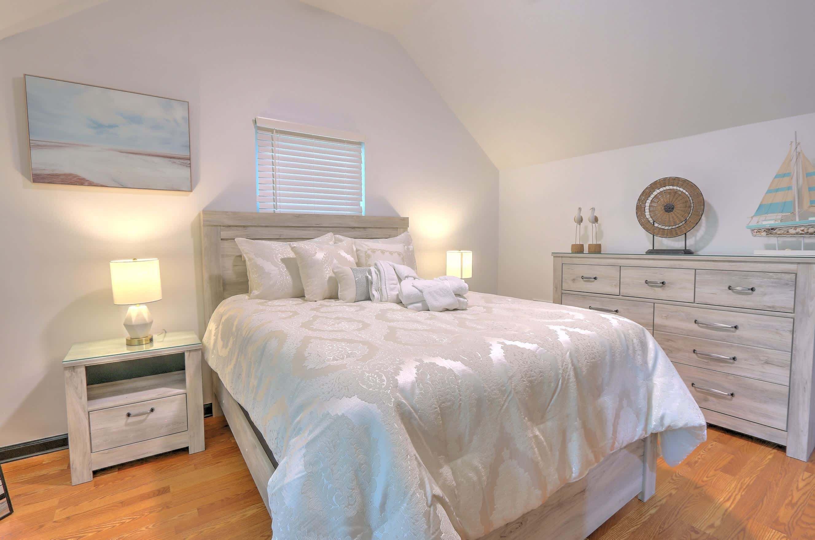 Quarto com cama, mesas de cabeceira, cômoda, janela e decoração de um veleiro fixado na parede.