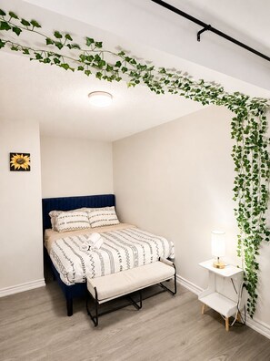 A bedroom with a bed, bench, bedside table, and wall-mounted plants.