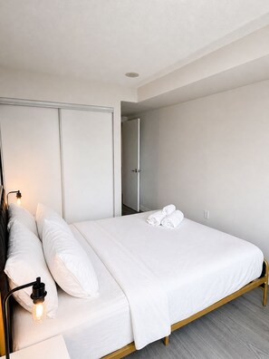 A modern bedroom with a single bed, white linens, a bedside table with a lamp, and a wardrobe.