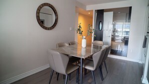 Een eethoek met een glazen tafel, zes stoelen, een vaas met bloemen en een ronde spiegel aan de wand.