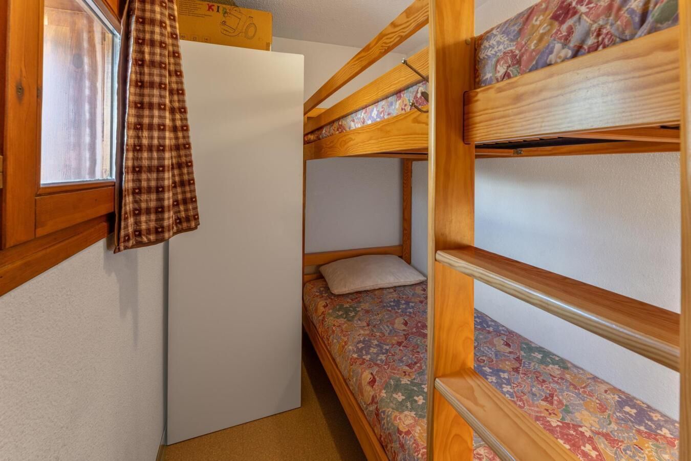 Une petite pièce avec des lits superposés, une petite fenêtre et une porte.