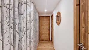 A hallway with wooden flooring, a wooden door at the end, and a wall with a tree pattern. - Cumaru-appartement-4pers-Proche Centre (Les Gets)