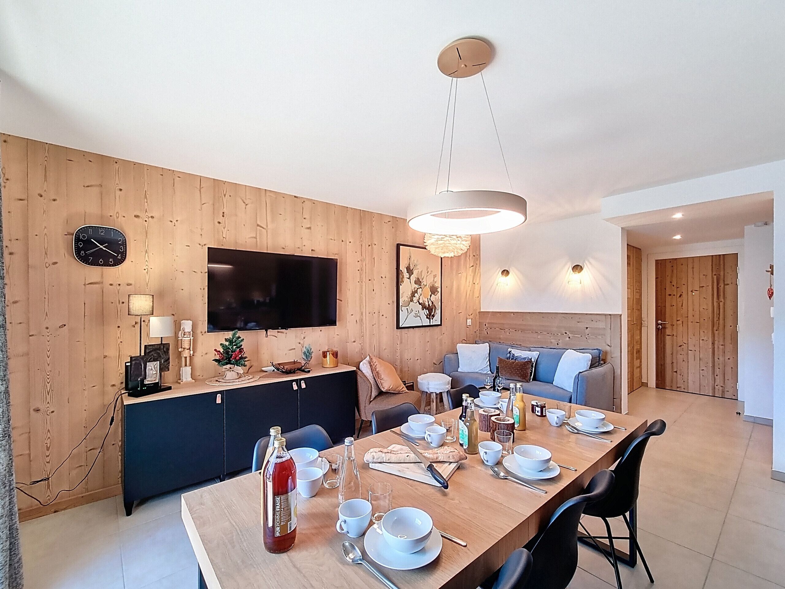 Een moderne keuken met een eettafel voor vier personen, een aan de muur bevestigde televisie en een wand van hout.