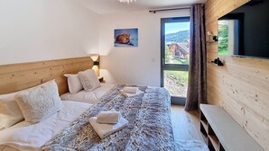 A bedroom with a large bed, a wooden headboard, a painting of a fox, a window with a view of a house, and a TV on the wall. - Cumaru-appartement-4pers-Proche Centre (Les Gets)