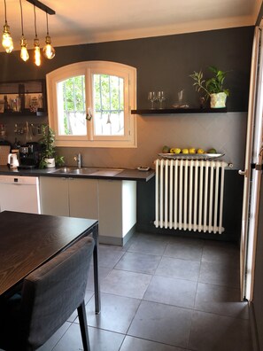 Moderni keittiö, jossa on keskeinen saareke, valkoiset kaapit, sisäänrakennettu uuni ja ikkuna, josta avautuu näkymä vehreään maisemaan.