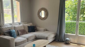Un salón con un sofá modular, una mesa de centro y ventanas amplias con cortinas.