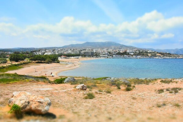 A coastal view with a sandy beach, clear blue water, and a cityscape in the background.