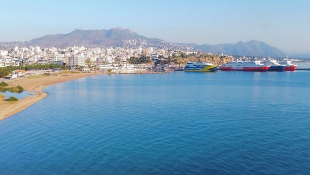 A coastal cityscape with a marina, buildings, and mountains in the background. - Cozy studio 50m from the beach of Rafina & 700m from the port (Rafina)