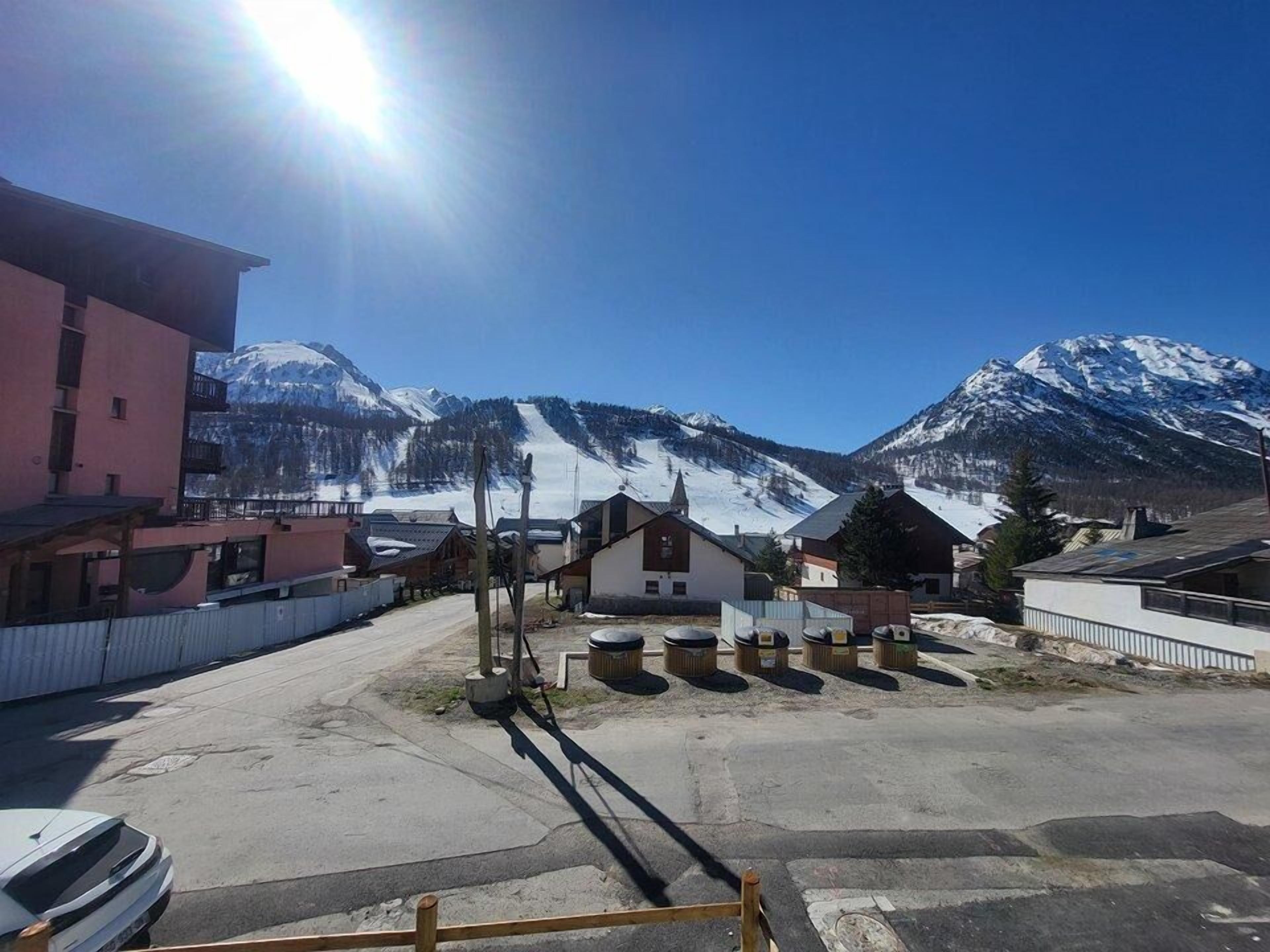A parking area with a row of buildings, a mountain backdrop, and a clear sky.