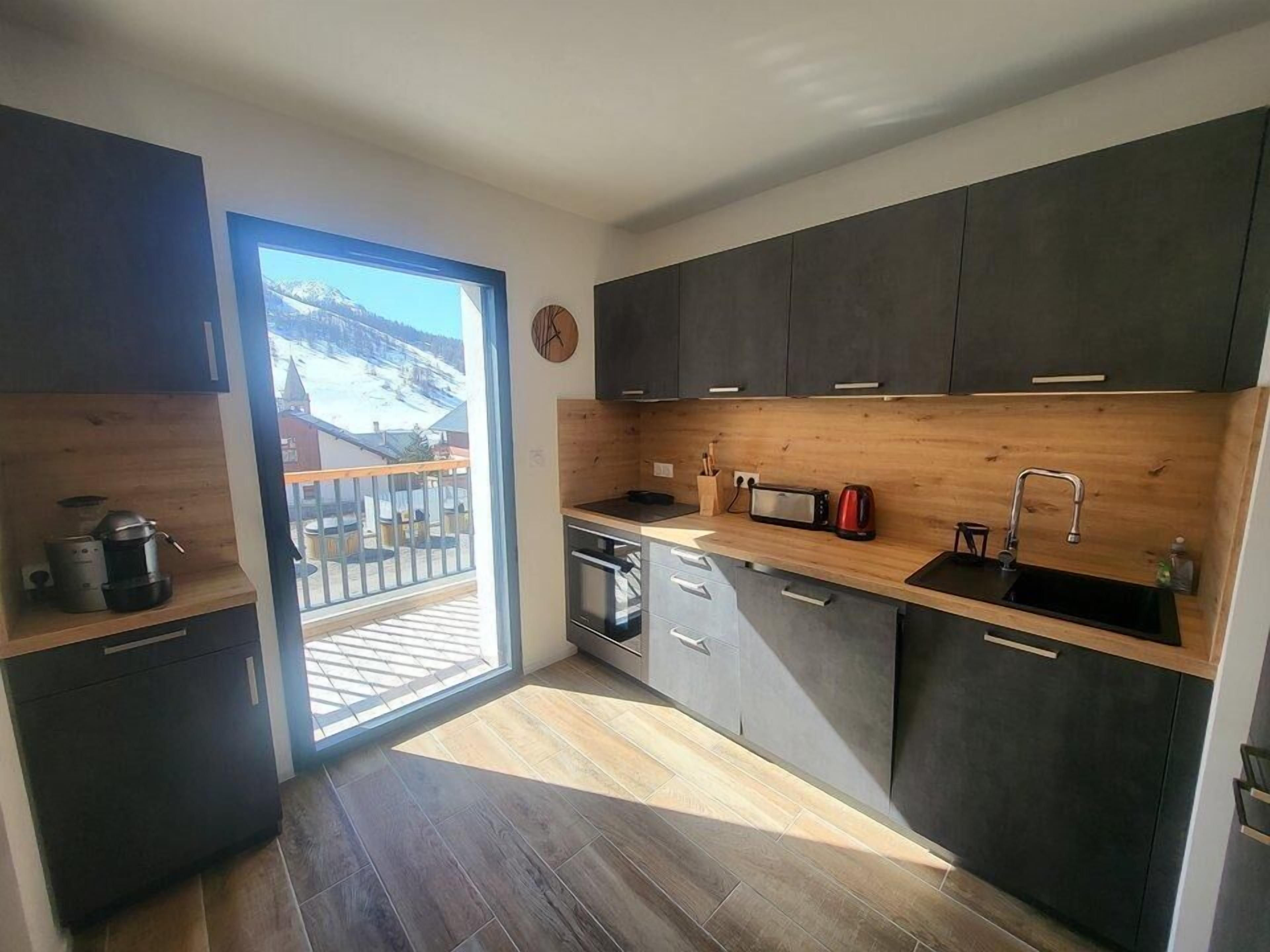 Eine moderne Küche mit dunklen Schränken, einer Holz Arbeitsplatte, einer Mikrowelle, einem Wasserkocher und einem Spülbecken.