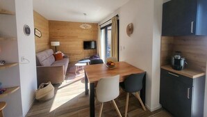 Un espacio habitable compacto con pared de madera, un sofá, una mesa de comedor con sillas, un televisor montado en la pared y una kitchenette con armarios.