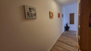 Un pasillo con suelo de madera, una lámpara en el techo y tres cuadros en la pared.