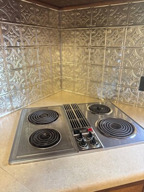 A kitchen with four burners, a red power button, and a vent hood.