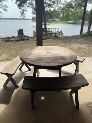 A wooden picnic table with benches, set on a concrete surface near a body of water with trees in the background. - DADS PLACE ON TOLEDO BEND LAKE (Many)