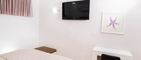 Un dormitorio con cama, un escritorio con silla, televisor y un cuadro en la pared.