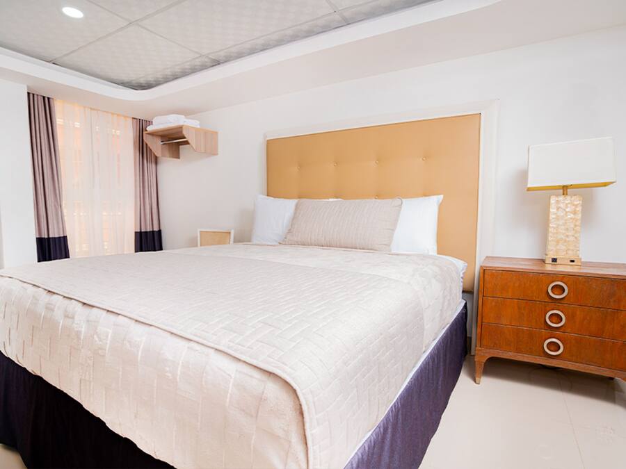 A spacious hotel room with a large bed, a wooden nightstand, and a bedside lamp.