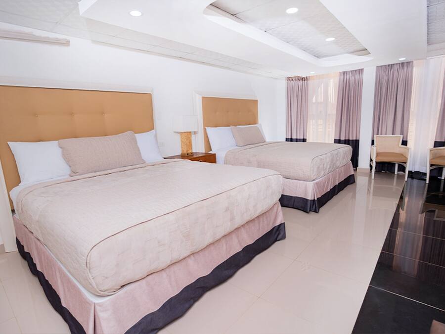 A hotel room with two beds, a nightstand, a chair, and a large window with curtains.