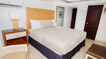 Een hotelkamer met een groot bed, een nachtkastje met een lamp, een houten bankje en een deur.