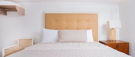 Une chambre d’hôtel bien aménagée, avec un grand lit, une tête de lit en bois, une table de chevet avec une lampe et une étagère intégrée.